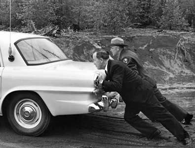 Senator Henry M. Jackson and Mt. Rainier Assistant Superintendent J. Leonard Volz pushing a KTNT radio news car out of the mud, Mount Rainier National Park, Washington, 1963
